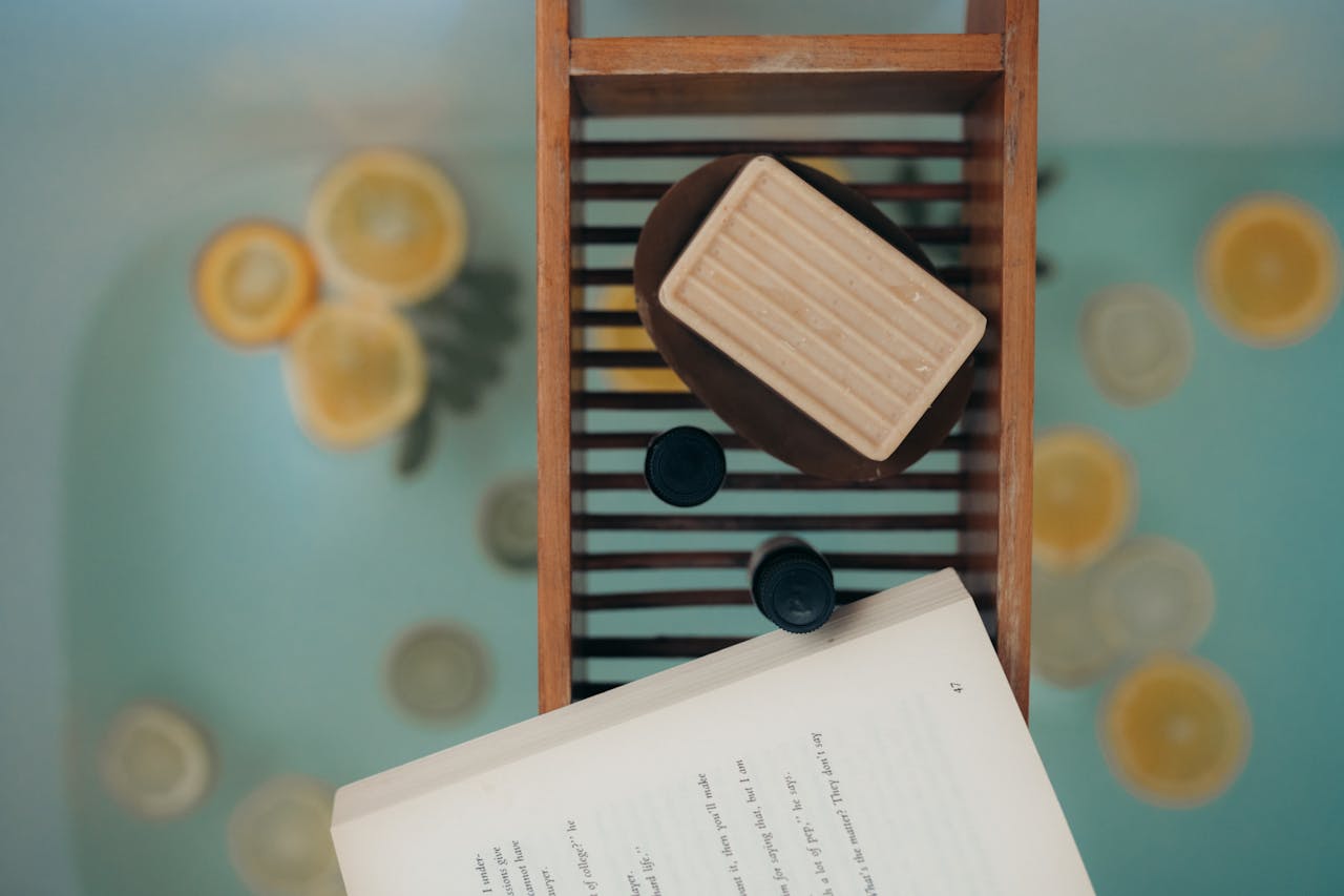 Top view of a calming bath scene with natural soap, citrus slices, and a book, ideal for relaxation.