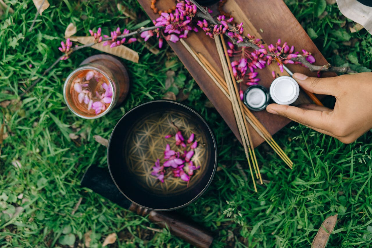 A tranquil setup featuring a singing bowl, incense, and flowers on grass for meditation and relaxation.