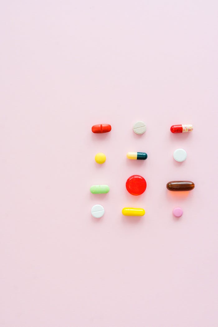 Vibrant assortment of pills and capsules arranged on a soft pink background.